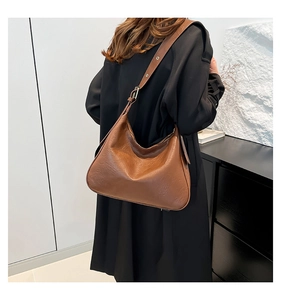 Brown leather hobo tote bag with adjustable strap worn by model on dark coat