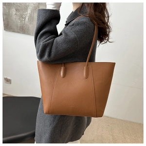 Detailed view of large brown lychee grain leather tote bag worn with a grey wool coat