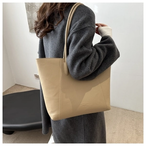 Detail of a large beige tote bag in lychee pattern leather worn over the shoulder