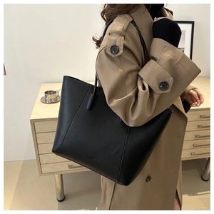 Close-up of minimalist black pebble leather tote bag worn with a classic khaki trench coat