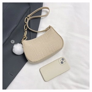 Detail der beigen Baguette-Tasche in Kroko-Optik mit Goldkette und weißem Plüsch-Anhänger