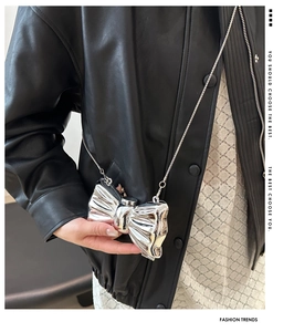Silver metallic bow crossbody bag with slim chain strap shown on a leather jacket