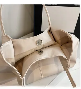 Detailed macro view of the glossy magnetic metal clasp on the beige leather tote bag