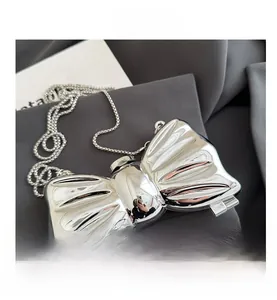 Detail of silver metallic bow-shaped evening clutch bag with beaded chain and textured finish