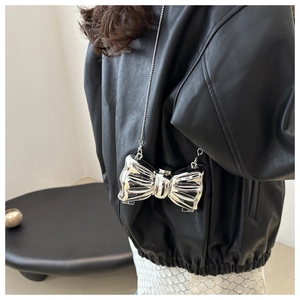 Detail of silver metallic bow-shaped mini bag with crossbody chain strap on model