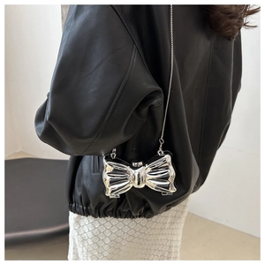Detail of silver metallic bow-shaped mini crossbody bag with delicate chain strap on model