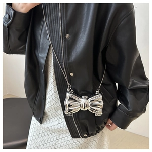 Metallic silver bow crossbody bag with chain strap styled on a leather jacket model