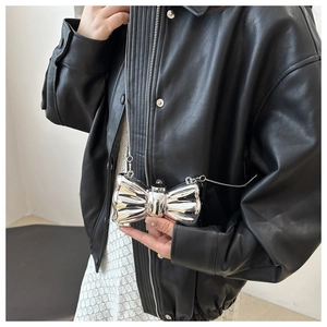 Detail of silver metallic bow-shaped chain bag held by a model in a cool modern style