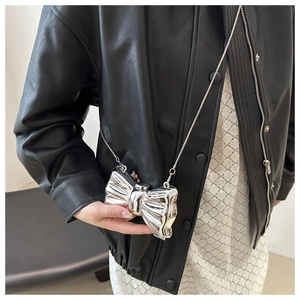 Detail shot of mini silver bow bag with liquid metal finish and chain on model