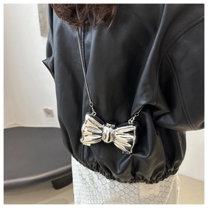 Detail of silver metallic bow-shaped mini bag with chain strap on leather jacket