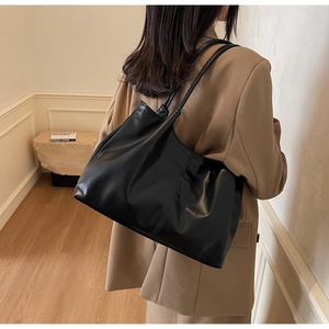 Detailed side view of large black tote bag worn with a camel blazer in minimalist setting