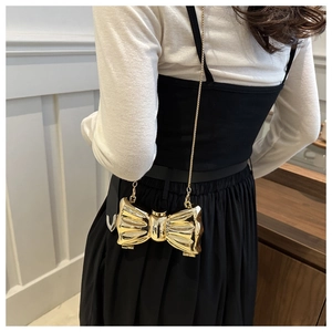 Detail of a mini gold bow crossbody bag featuring a glossy metallic finish and chain strap