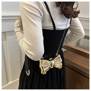 Close-up of golden bow-shaped crossbody bag with high-gloss finish and fine chain strap