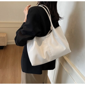 Detail of a large white tote bag with vertical stitching on a black blazer outfit