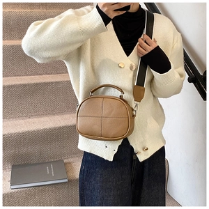 Brown litchi grain crossbody bag with wide striped strap and top handle shown on model