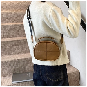 Close-up of brown textured leather crossbody bag with cross-stitch and wide strap