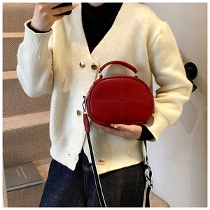 Detail of red leather crossbody bag with cross-stitch pattern and woven shoulder strap