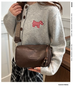 Detail der dunkelbraunen Boston-Tasche mit Logo-Prägung, Quaste und Vintage-Gurtband