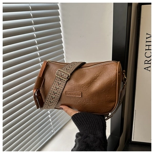 Nahaufnahme der braunen Zylindertasche mit Retro-Falten und breitem Ethno-Schultergurt