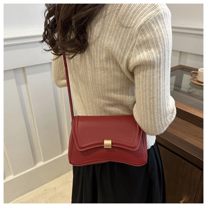 Detail of red leather crossbody bag with gold buckle worn on the side over a chic outfit
