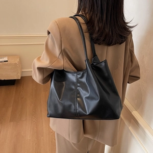 Minimalist black tote bag in soft glossy faux leather shown on shoulder with blazer