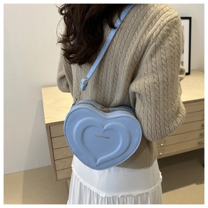 Détail du sac bandoulière bleu clair en forme de cœur avec texture sur pull en maille