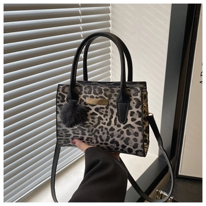 Détail du sac léopard avec plaque métallique dorée et pompon décoratif en fourrure noire