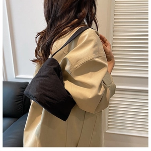 Détail d'un sac à bandoulière noir en tissu plissé porté avec une veste beige élégante