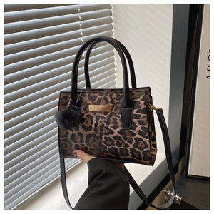 Détail du sac à main léopard avec pompon en peluche noire et plaque en métal doré