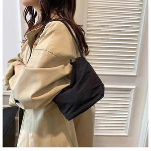 Sac à bandoulière plissé noir minimaliste porté à l'épaule sur un mannequin en trench-coat