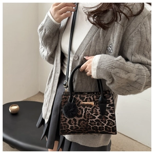 Détail du sac à main imprimé léopard avec plaque dorée et breloque pompon en fourrure noire