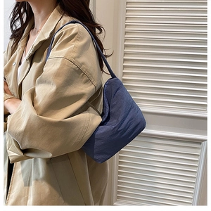 Détail d'un sac à bandoulière plissé bleu foncé porté par un mannequin en trench-coat