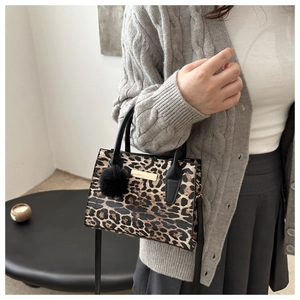 Sac bandoulière chic à motif léopard avec pompon noir et détails dorés sur modèle