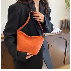 Gros plan d'un sac nuage plissé orange vif avec tissu texturé porté sur un tailleur noir