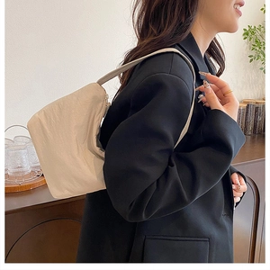 Détail du sac hobo plissé crème porté à l'épaule dans un cadre intérieur chaleureux