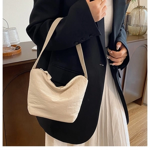 Gros plan du sac hobo plissé beige minimaliste porté comme sac à bandoulière sous le bras