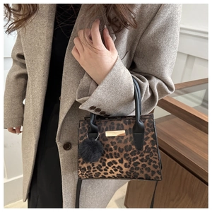 Détail du sac léopard avec garnitures dorées et pompon noir sur une veste chic