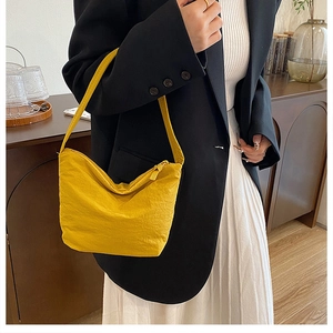 Modèle portant un sac bandoulière jaune plissé avec blazer noir et jupe blanche