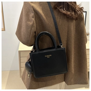 Detail of black crossbody bag with round coin purse and gold lettering on brown coat