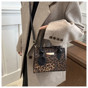 Sac à bandoulière léopard avec détails dorés et pompon noir sur manteau beige