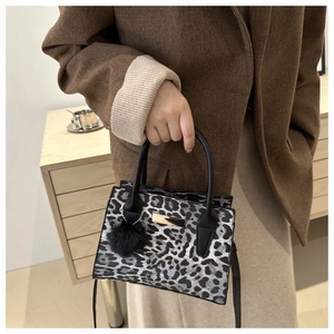 Détail du sac à main léopard avec plaque en métal doré et pompon en fourrure noire