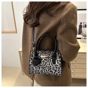 Détail d'un sac à main léopard avec ferrures dorées et pompon sur un blazer marron