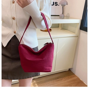 Gros plan d'un sac hobo plissé bordeaux en tissu porté sur un pull en maille blanche
