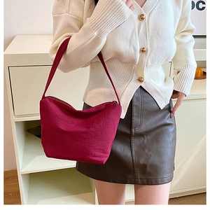 Gros plan d'un sac hobo plissé bordeaux porté avec un cardigan et une jupe en cuir