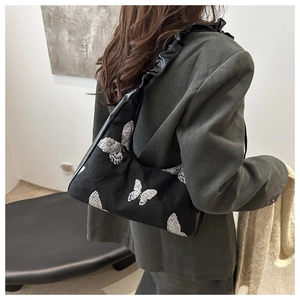 Detail view of black underarm bag with silver butterfly embroidery and ruffled strap