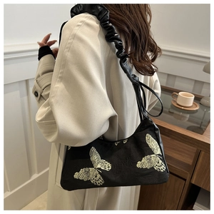 Close-up of black butterfly embroidery detail on underarm bag with ruffled strap