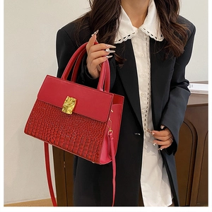 Detail of red crocodile texture handbag with gold buckle shown on a female model