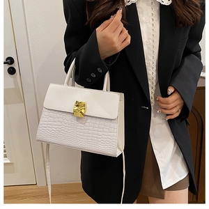 Detail of white crocodile-embossed leather handbag with decorative gold wavy metal buckle