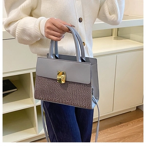 Detail of grey-blue handbag featuring crocodile texture and golden metal twist lock