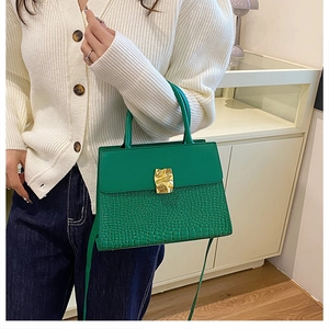 Détail du sac à main vert foncé avec motif crocodile, fermoir doré et poignée supérieure